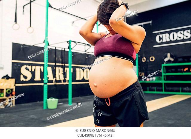 Pregnant woman holding head in hand in gym