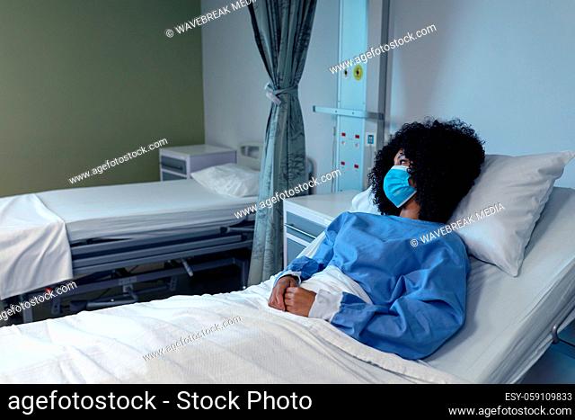 African american female patient lying in hospital bed wearing face mask