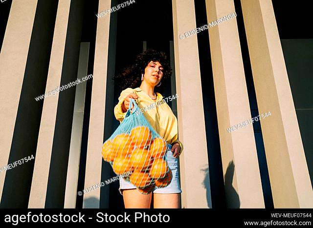 Young woman with oranges in mesh bag in front of column