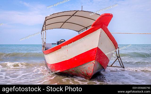 Longtail boat with red and white stripes waiting for passengers on beautiful monkey beach in Penang national park, Malaysia