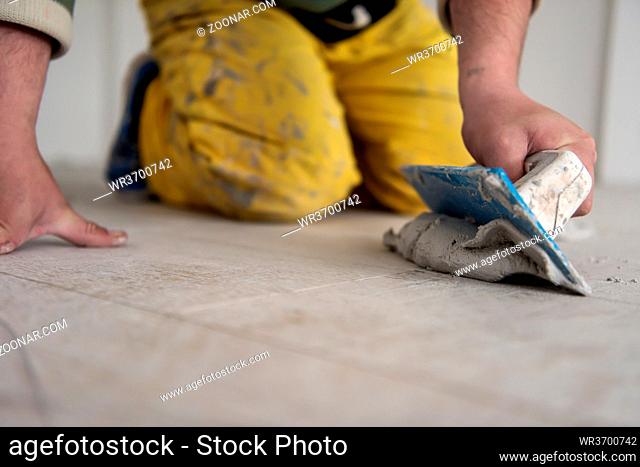 Grouting ceramic tiles. Tilers filling the space between ceramic wood effect tiles using a rubber trowel on the floor in new modern apartment