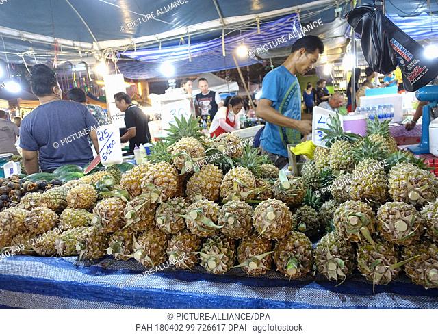 04 March 2018, Thailand, Karon Beach: A dealer sells pineapples and other fruit at the temple market in Karon Beach. The two-week temple market takes place...