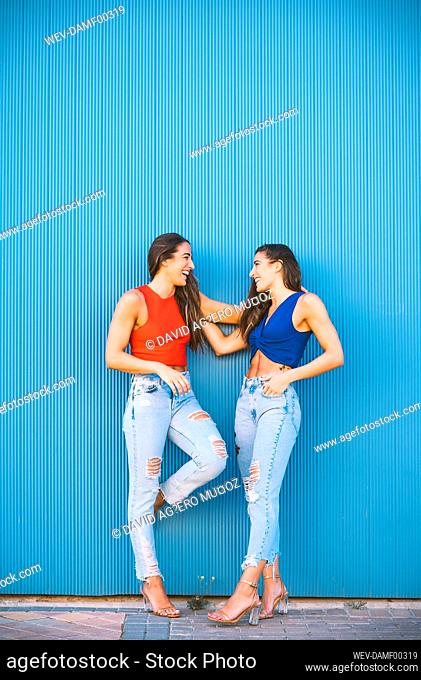 Smiling twins leaning on blue wall