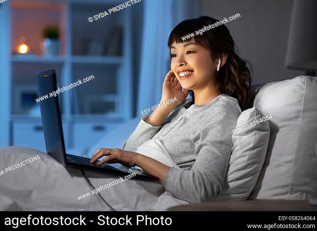 woman with laptop and earphones in bed at night