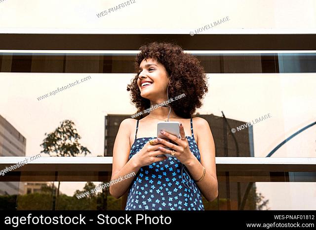 Young woman with in-ear headphones and mobile phone looking away