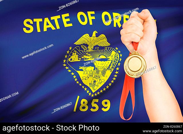 Sportsman holding gold medal with State of Oregon flag on background. Part of a series