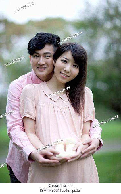 Young man and pregnant woman holding a pair of baby shoes with smile together