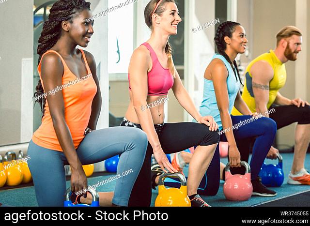 Full length of three young and beautiful determined people holding kettlebells while exercising Russian swing during functional training class at the gym