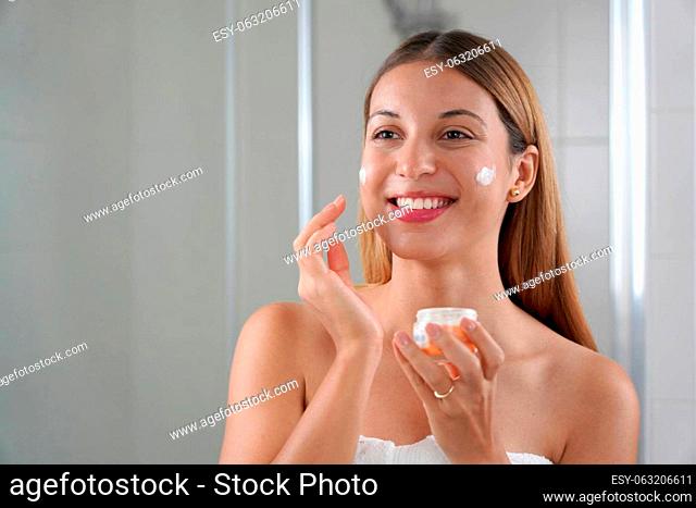 Young woman applying cream on her cheeks. Wellness treatments for teenage sensitive skin concept