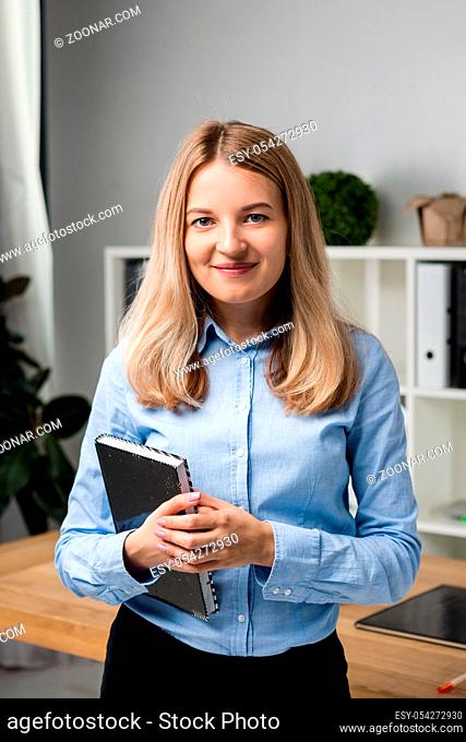 Businesswoman Holding Large File. young womanl standing in the office and holding folder. Portrait of young office worker holding folders of paperwork while...