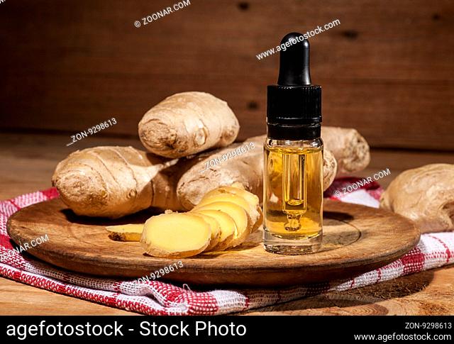 Oil of ginger in a small glass bottle macro and root on wooden table