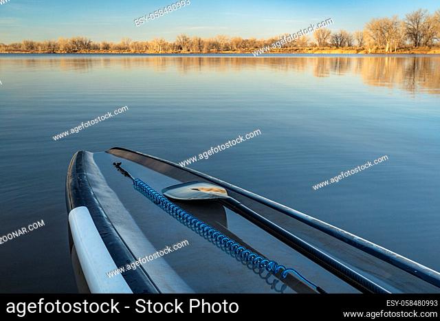 touring stand up paddleboard with a safety leash and paddle on a calm lake in early spring scenery in northern Colorado