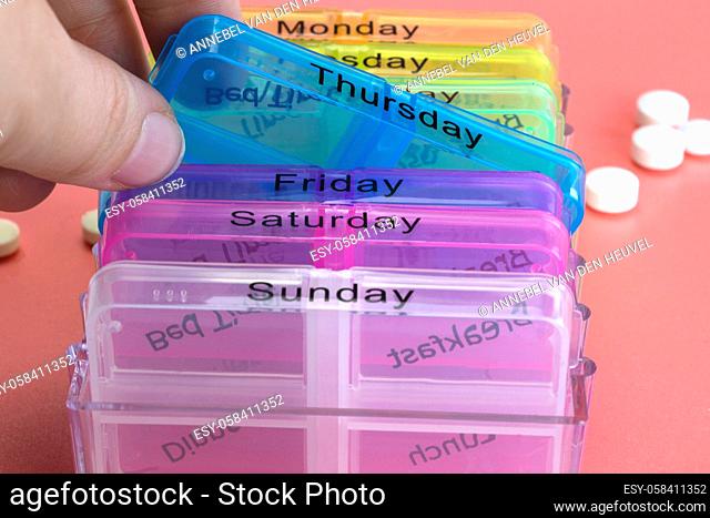 Pill box reminder, hand taking medicine daily pills in colorful box on pink background, elderly, senior, business, health