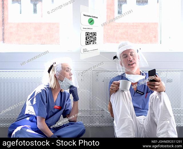 Doctors wearing personal protective equipment looking at cell phone with Covid-19 vaccine certificate