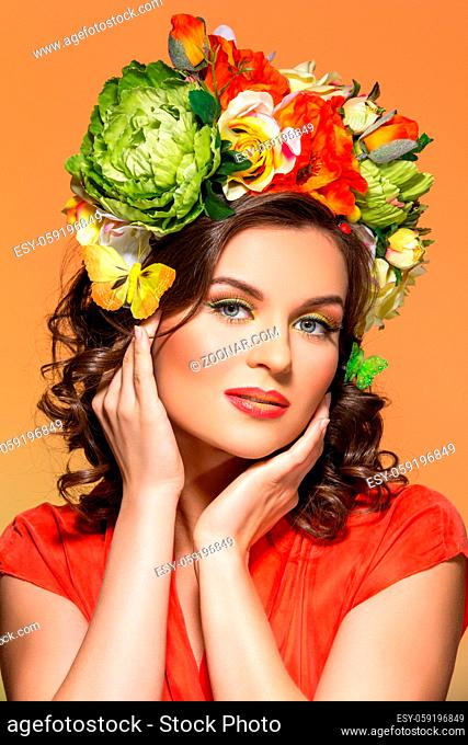 beautiful young woman in orange dress with flowers in hair. Studio shot on yellow background. Copy space