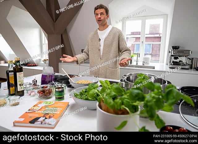 05 October 2023, Bavaria, Munich: National soccer player Thomas Müller speaks and gestures at a stove during the presentation of the cookbook ""Kochen für...