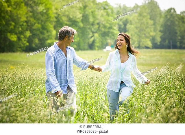 Mature man and a mid adult woman holding hands and running in a field