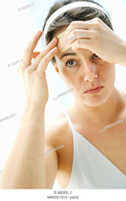 young woman is sticking a plaster onto her forehead -band-aid