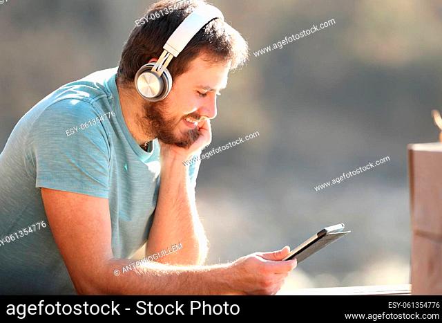 Happy man with wireless headphones watching media content on tablet outdoors