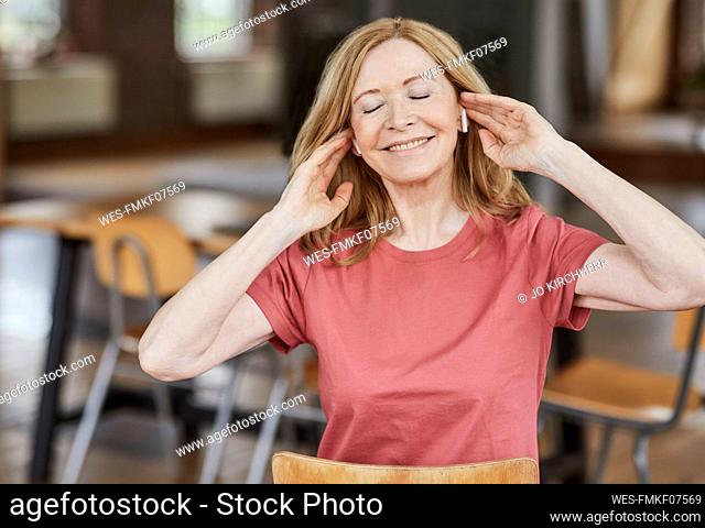 Smiling woman wearing wireless in-ear headphones enjoying music at home