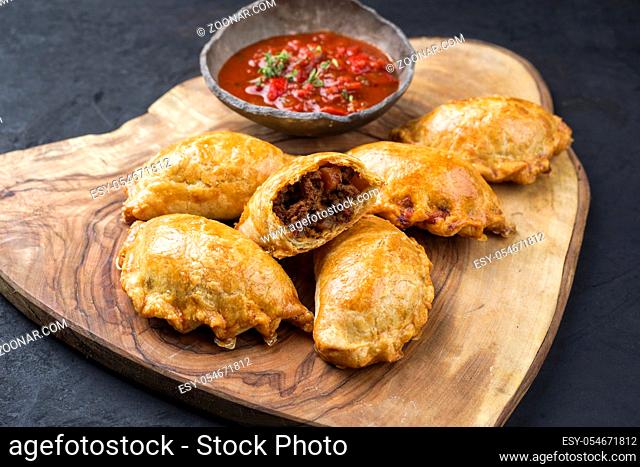 Traditional South American empanada de carne offered with a chili dip as closeup on a rustic wooden board