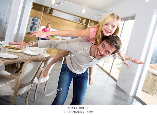 Mature man giving daughter piggy back in dining room