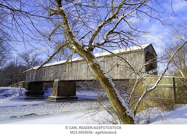 A bare tree, snow and an old wooden covered bridge, Pennsylvania, USA
