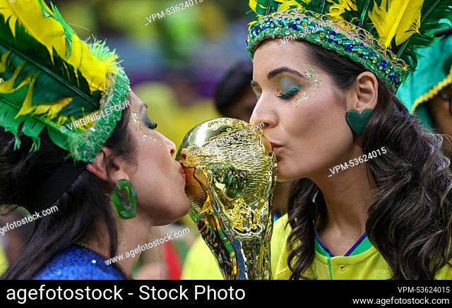 Brazilian supporters, two women wearing yellow and green feathers on their heads, kiss a fake world cup during a soccer game between Brazil and Serbia