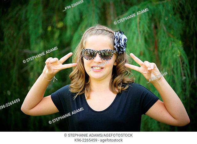 young girl smiling at the camera wearing sunglasses with peace sign fingers