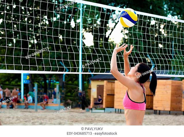 Slender brunette woman playing volleyball near the net on the beach. Space for text