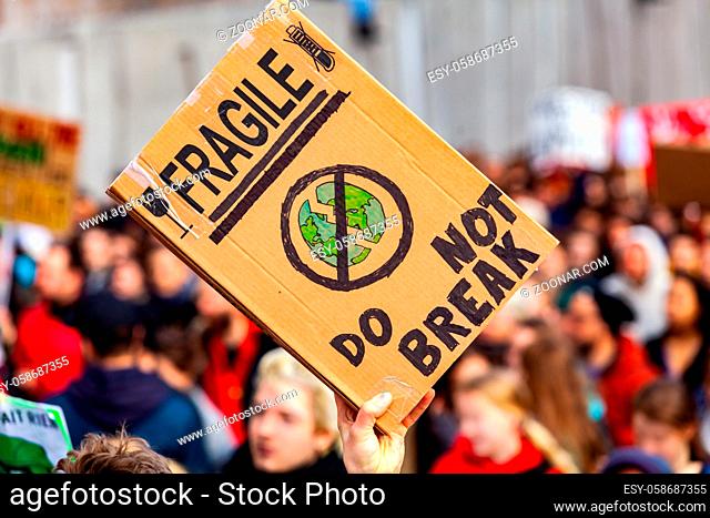 A homemade cardboard sign is seen close up, showing that planet earth is fragile, do not break, as eco-friendly protestors march on a city street