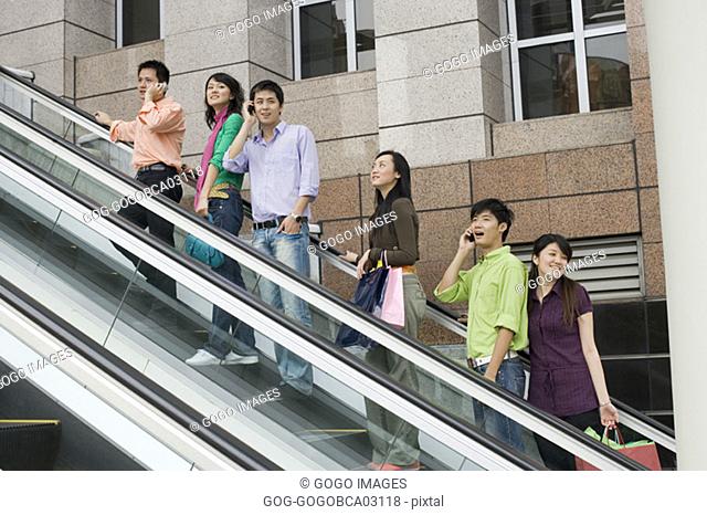 Young men talking on cell phones while riding an escalator