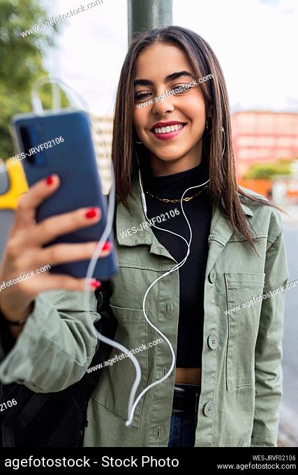 Smiling woman with in-ear headphones using mobile phone