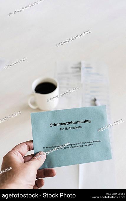 Hand of man holding ballot paper over coffee cup