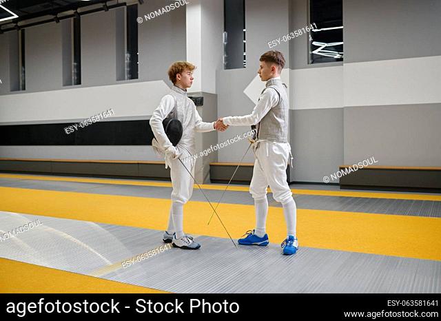 Professional fencers shaking hand after or before fencing match. Athletes in uniforms protective helmet mask greeting or thanking each other at martial art...