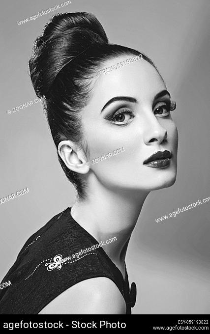 Beautiful young woman with hairdo and bright make-up. Doll style. Beauty shot on grey background. Copy space. Monochrome