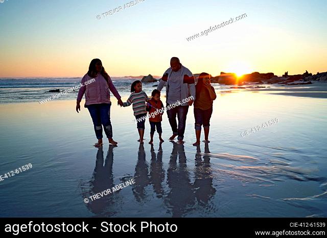 Family holding hands in wet sand on beach at sunset