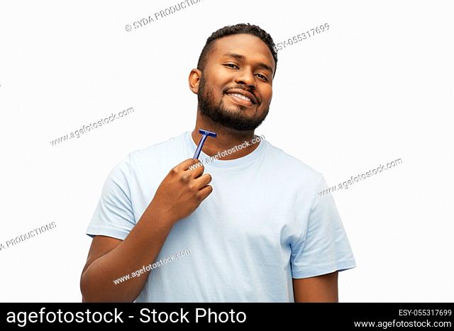 smiling african man shaving beard with razor blade