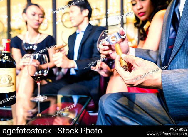 Asian Man sitting with friends and cutting cigar