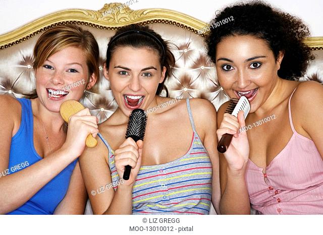 Teenage Girls using brushes as microphones singing at Slumber Party