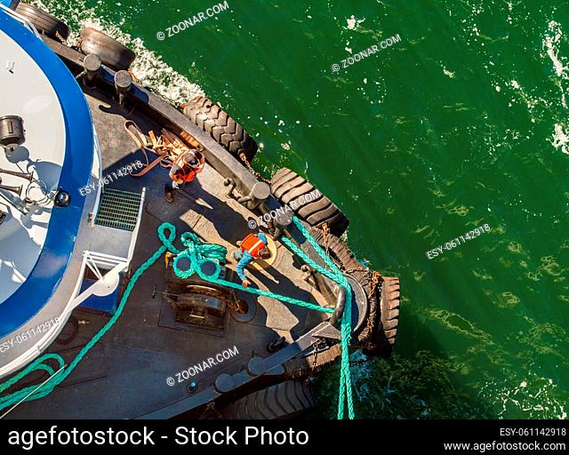 Overhead POV view of tugboat, ropes and workers assisting large ship to dock in high winds on a bright sunny day. Gastineau Channel, Juneau, Alaska, USA