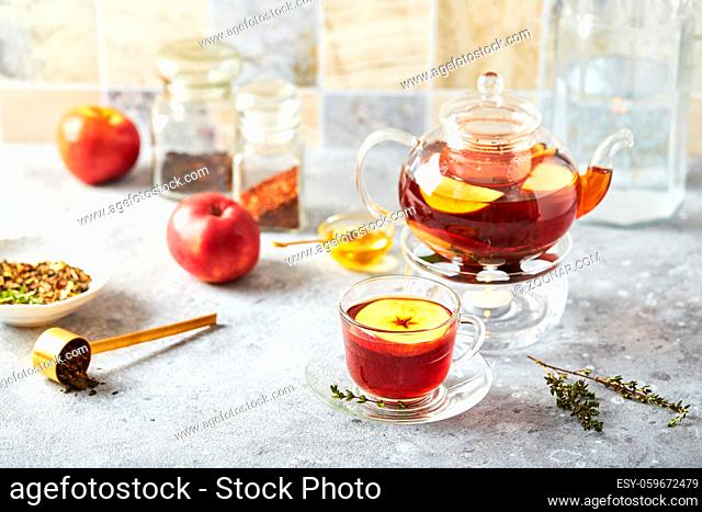 Fruit tea with apples and thyme in glass teapot and cup on the kitchen table
