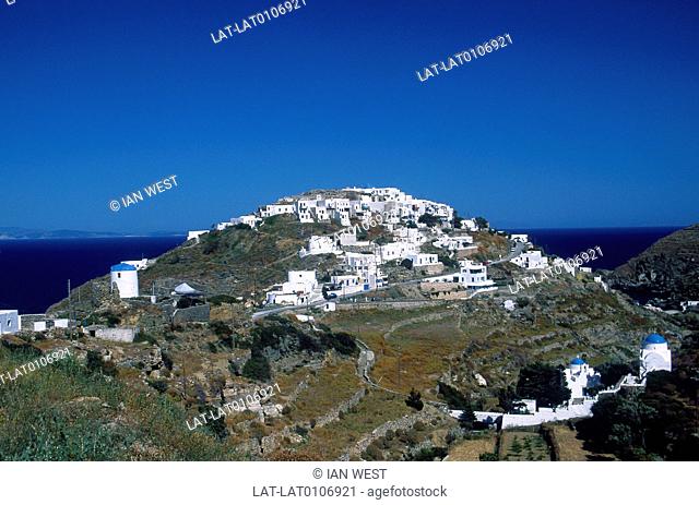 Cyclades Islands. Hilltop town. White houses, buildings. Blue domes of church. Paths winding on hillside