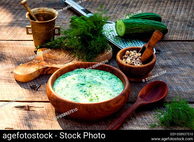 Homemade chilled tarator with ingredients on wooden rustic background. Traditional bulgarian summer cold soup with cucumbers, dill, garlic, yogurt and walnuts