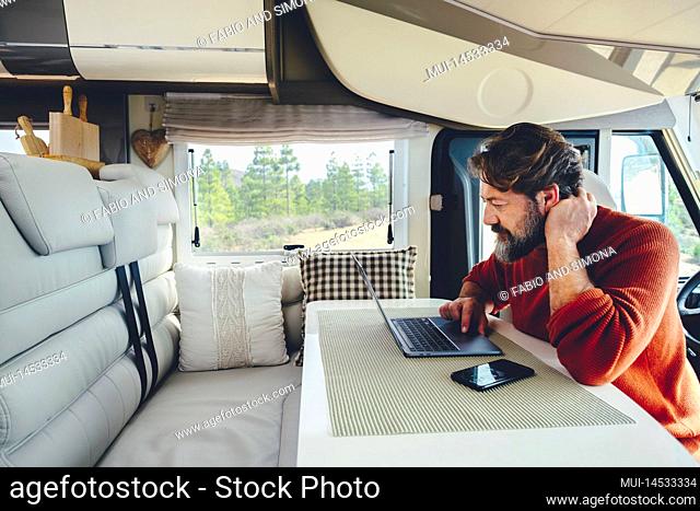 Young modern adult man work on laptop computer in remote working and digital job lifestyle inside a modern and connected camper van with nature woods view...