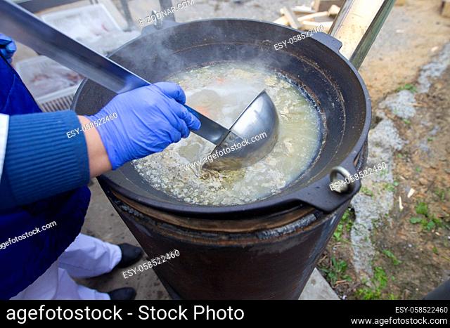The chef's hand is filling the soup with a large scoop from a vat or saucepan. Street food