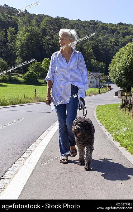 Europe, Luxembourg, Septfontaines, Older woman walking her Pet Portuguese Water Dog through the Eisch Valley