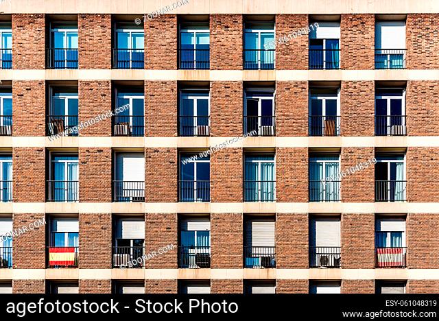 Full frame of brick facade of residential building with array of rectangular windows, some of them with Spanish flag