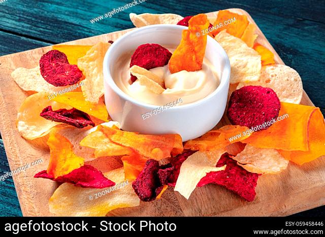 Vegetable chips with a dip on a wooden board, a healthy vegan snack