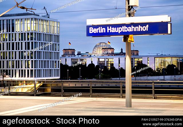 27 September 2021, Berlin: A sign reading ""Berlin Hauptbahnhof"" stands on a platform, while the Reichstag building and the Paul Löbe House are brightly lit in...